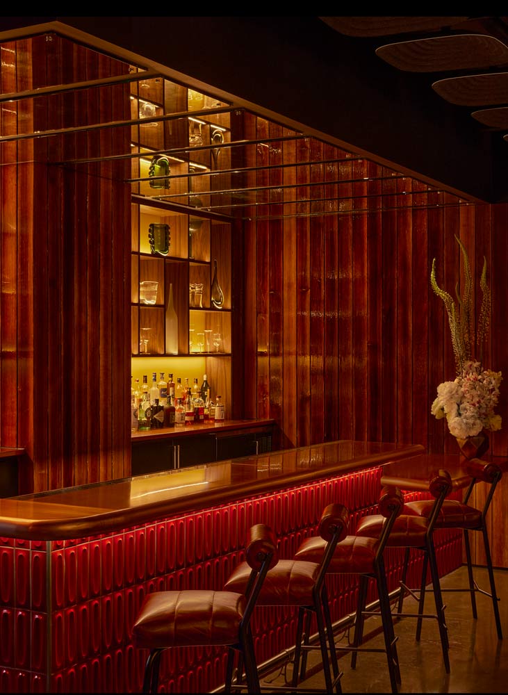 A bar inside AMA by Brad Kilgore offers red chairs and wooden walls for a high-energy dining experience.